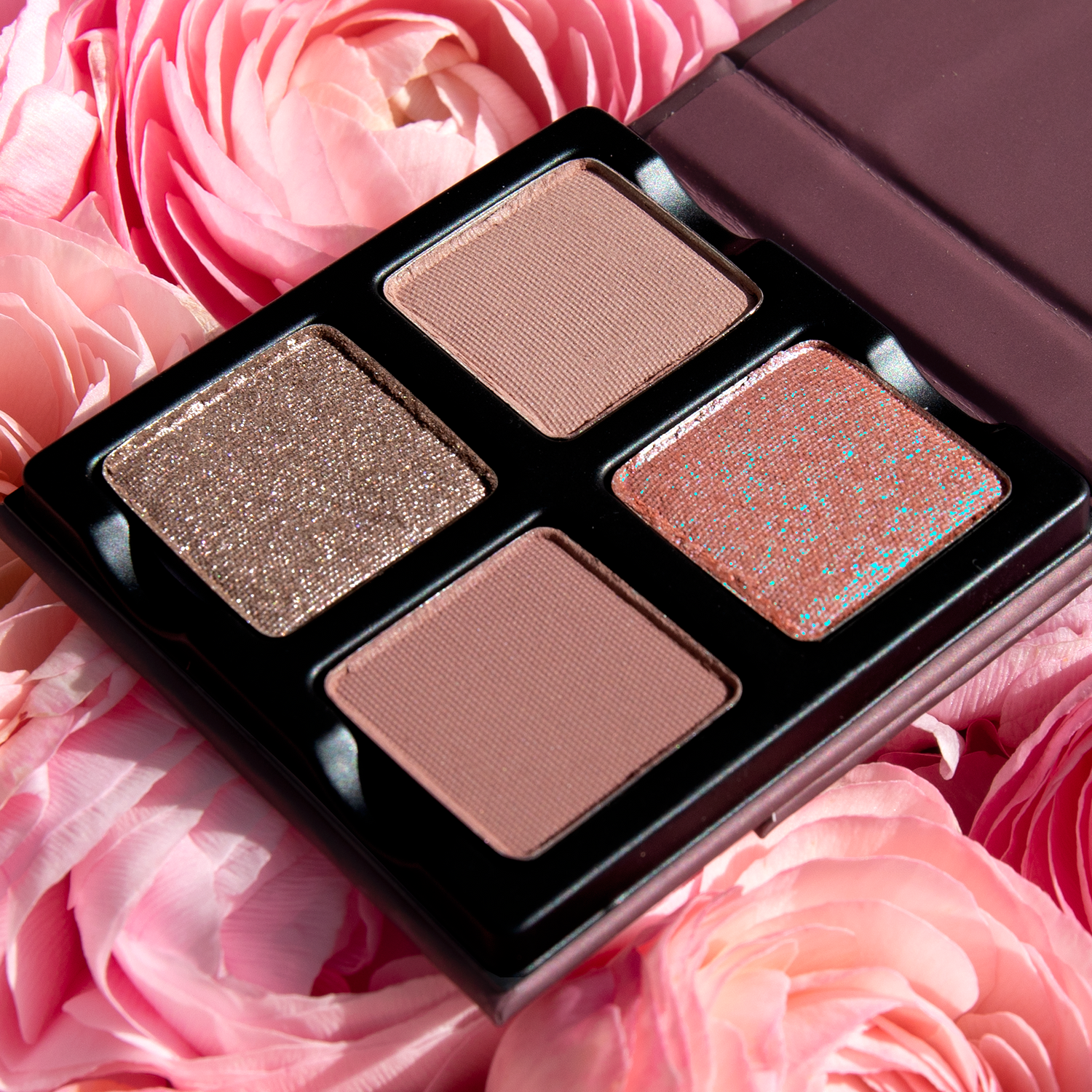 Open Petits Fours - Hesperides 4-pan palette on a background of roses showcasing pressed powders in rose, mauve, and nude tones