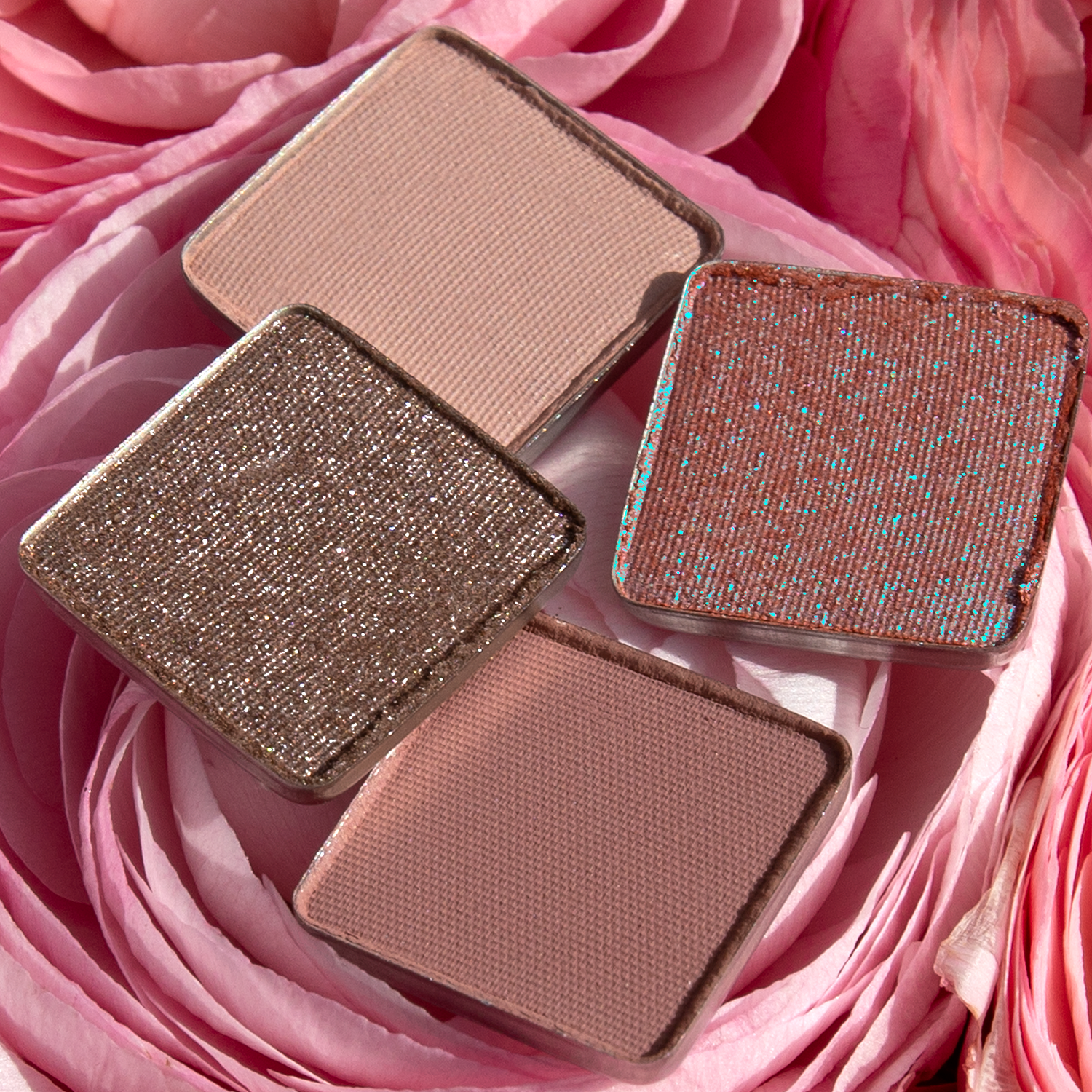 Single shades of pressed powders from the Petit Fours - Hesperides collection in rose, mauve, and nude tones, resting in roses.