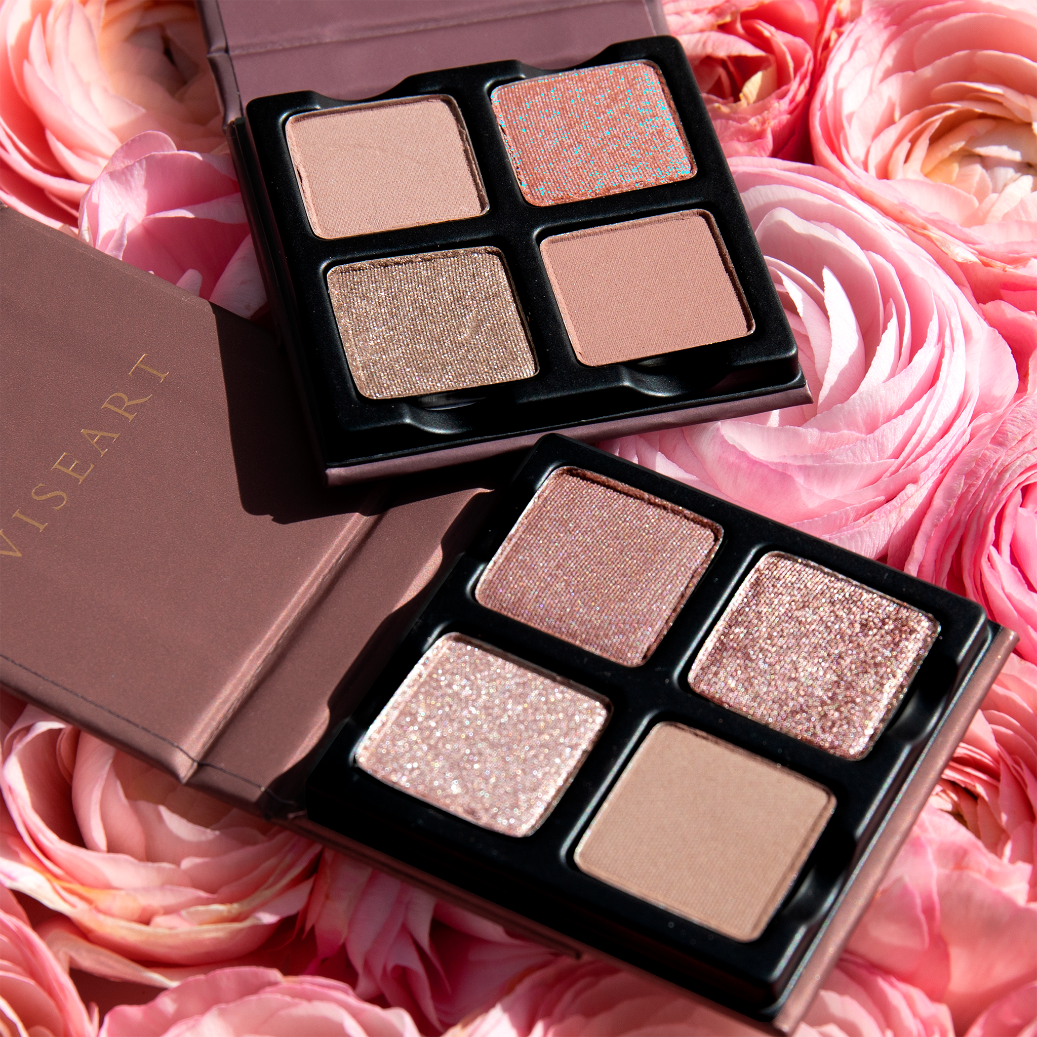 Two open Petits Fours - Isolde 4-pan palettes layered on a background of roses showcasing pressed powders in rose, nude shimmer, and soft satin tones.