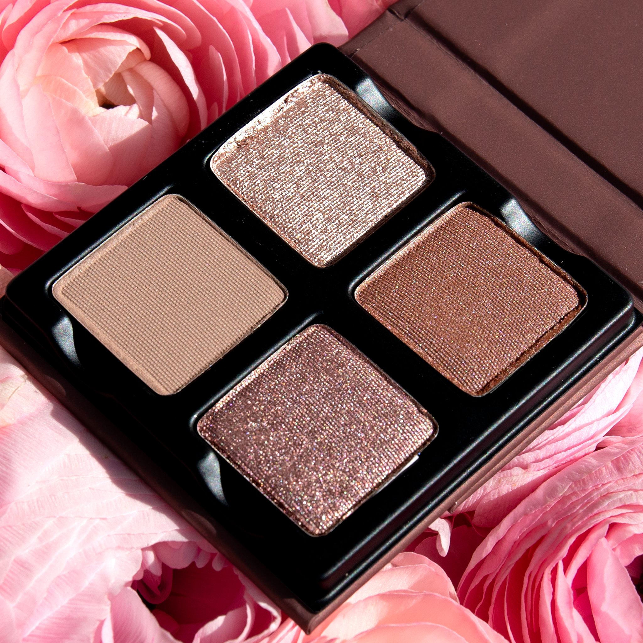 Open Petits Fours - Isolde 4-pan palette on a background of roses showcasing pressed powders in rose, nude shimmer, and soft satin tones.