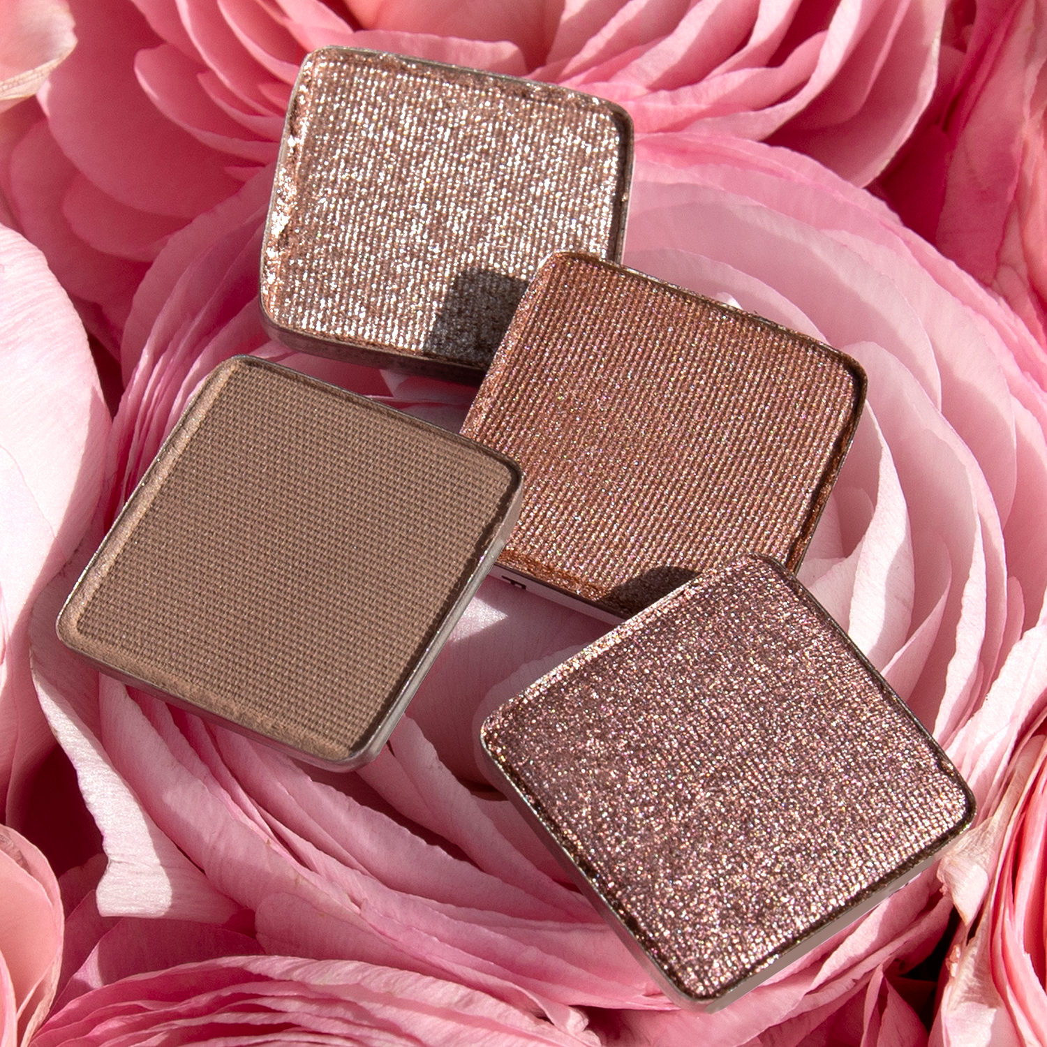 Single shades of pressed powders from the Petit Fours - Isolde collection in rose, nude shimmer, and soft satin tones, resting in roses.