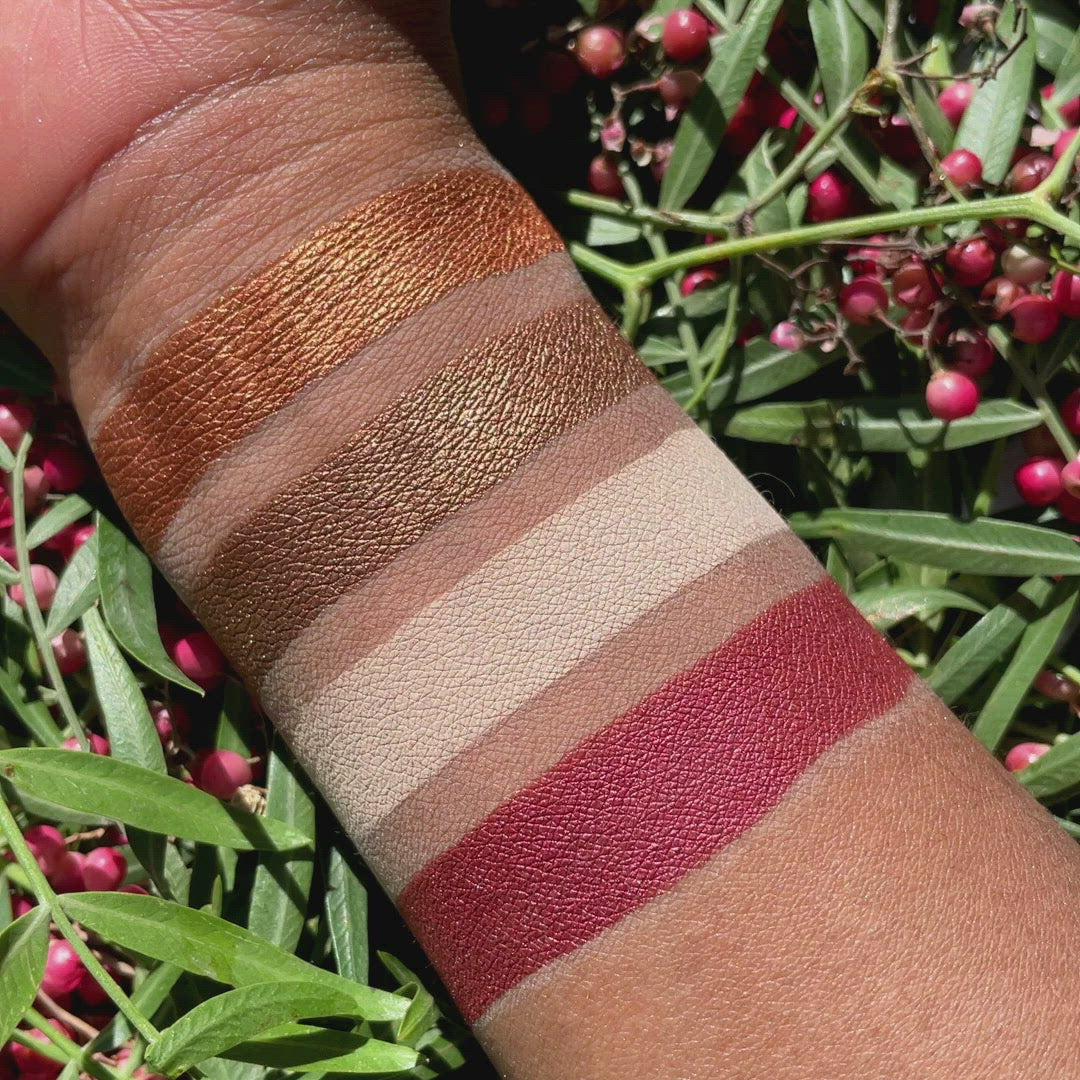 Swatches of Petits Fours Garnet on deep skin, highlighting warm red matte, plum shimmer, and wine satin