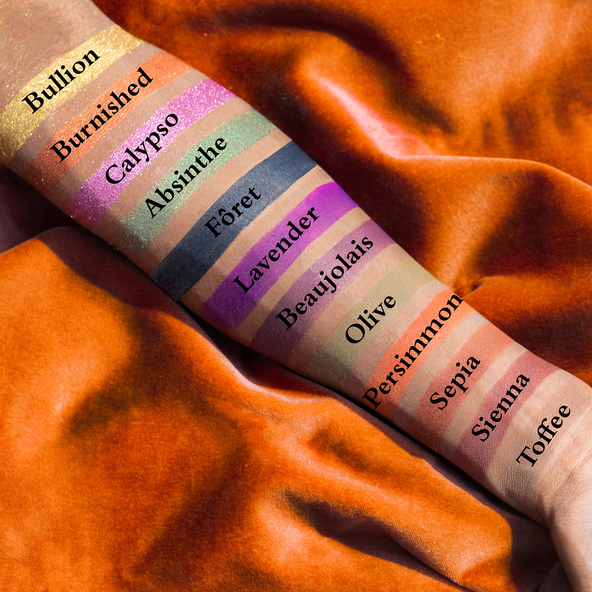 Swatches of emerald, copper, plum, and gold shades from mini palette on deep skin tone.