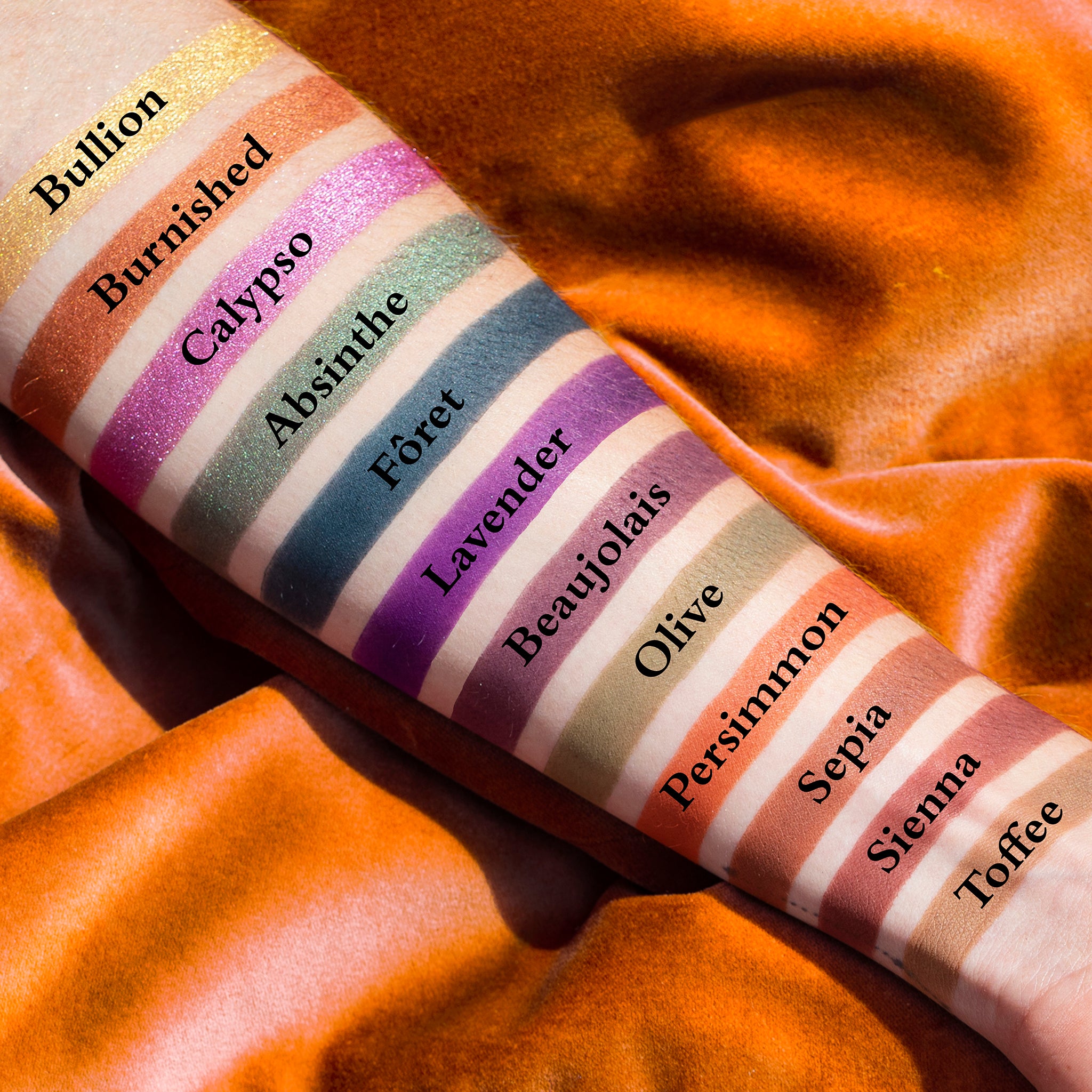 Swatches of emerald, copper, plum, and gold shades from mini palette on fair skin tone.