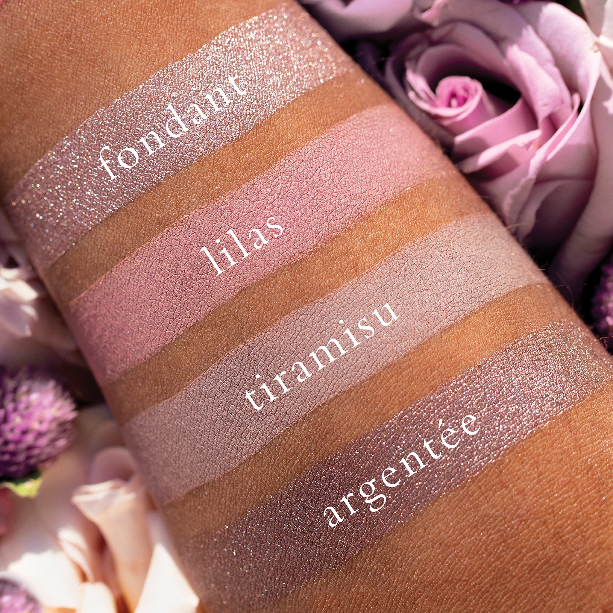 Swatches of Petits Fours Lilas on deep skin, showing pastel lilac, mauve shimmer, and soft plum tones.