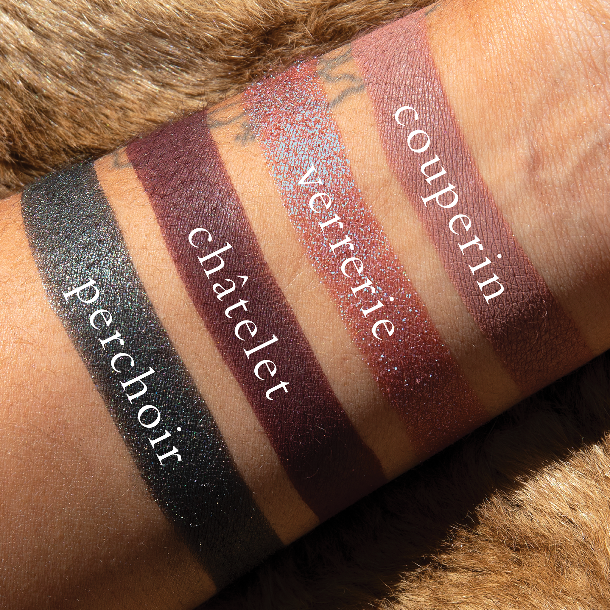 Swatches of Petits Fours Violetta on deep skin, revealing plum duochrome, deep berry, and soft gunmetal.