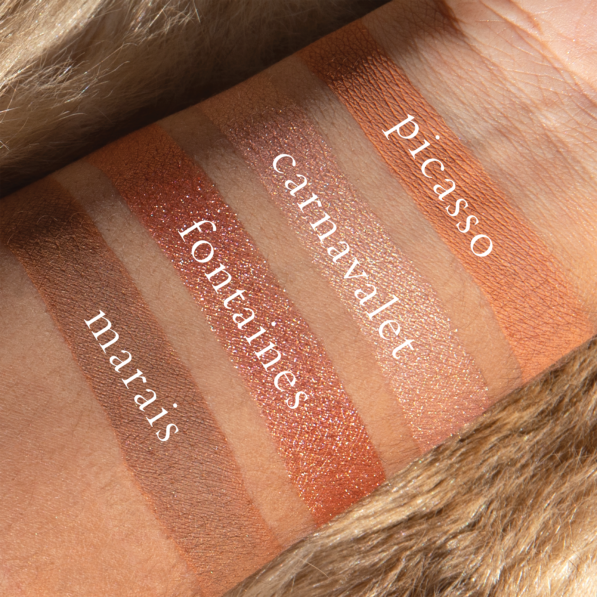 Swatches of blush satin, pale peach matte, and champagne shimmer from Amélie on deep skin tone.
