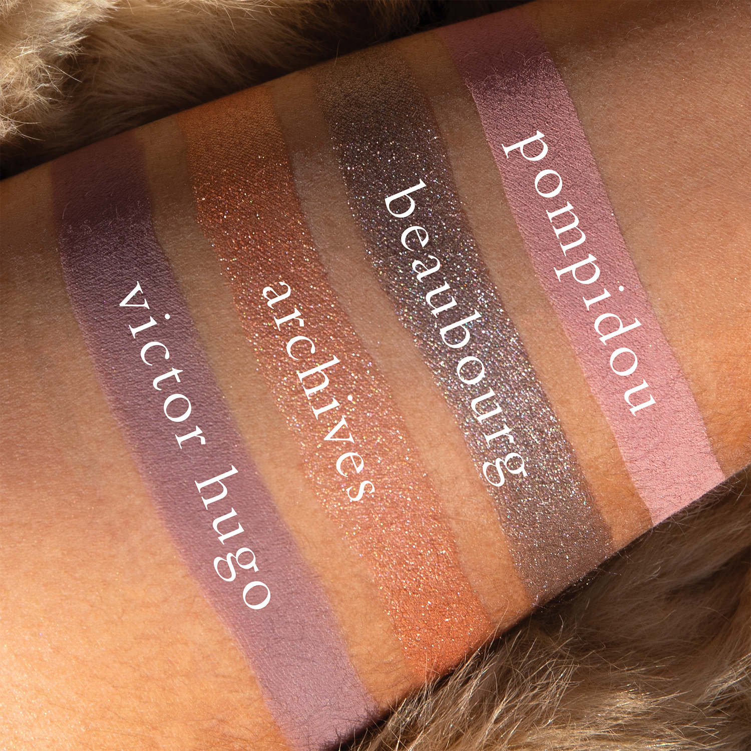 Swatches of Petits Fours Lilas Deux on deep skin, showing plum matte, soft lavender shimmer, and taupe grey.