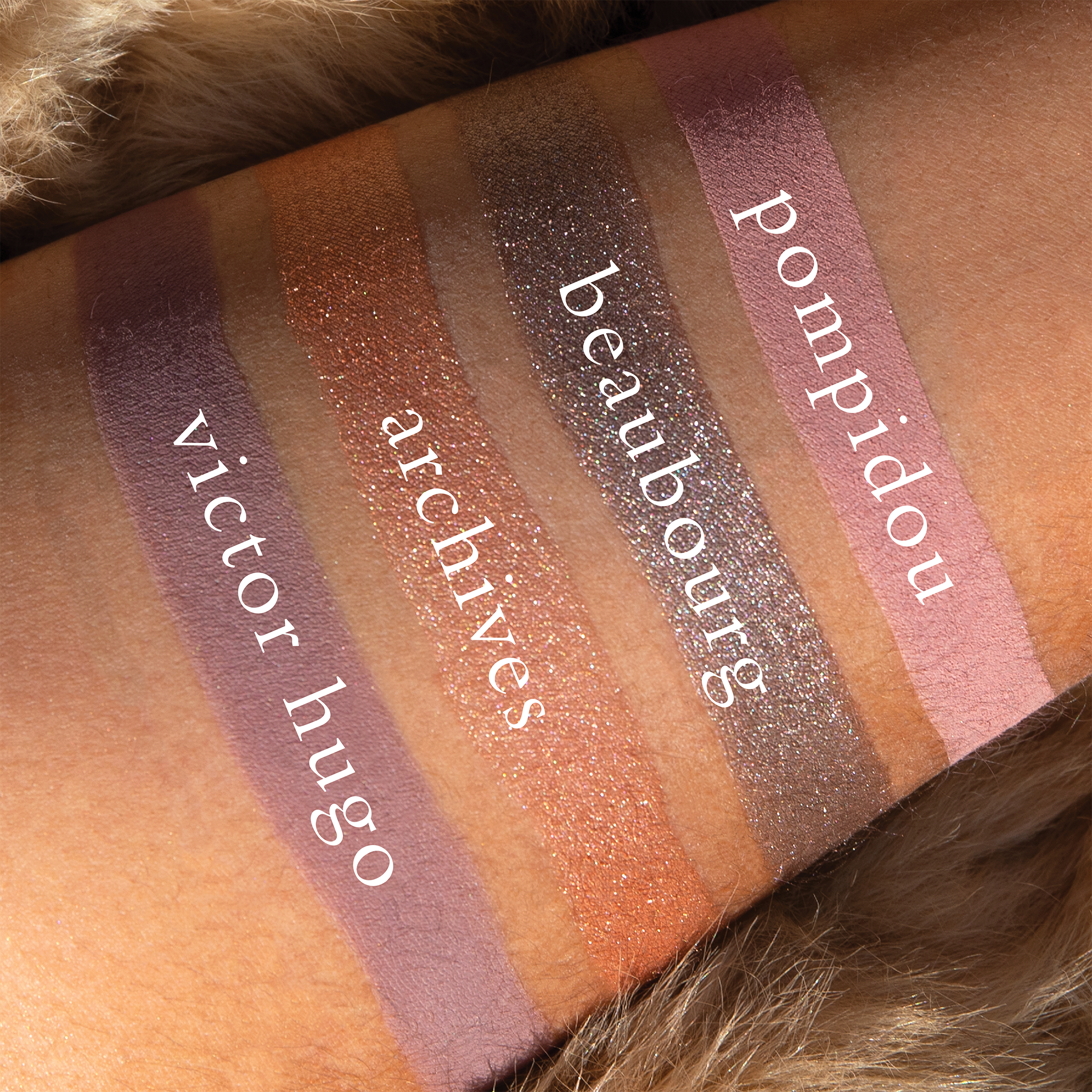 Swatches of Petits Fours Lilas Deux on deep skin, showing plum matte, soft lavender shimmer, and taupe grey.