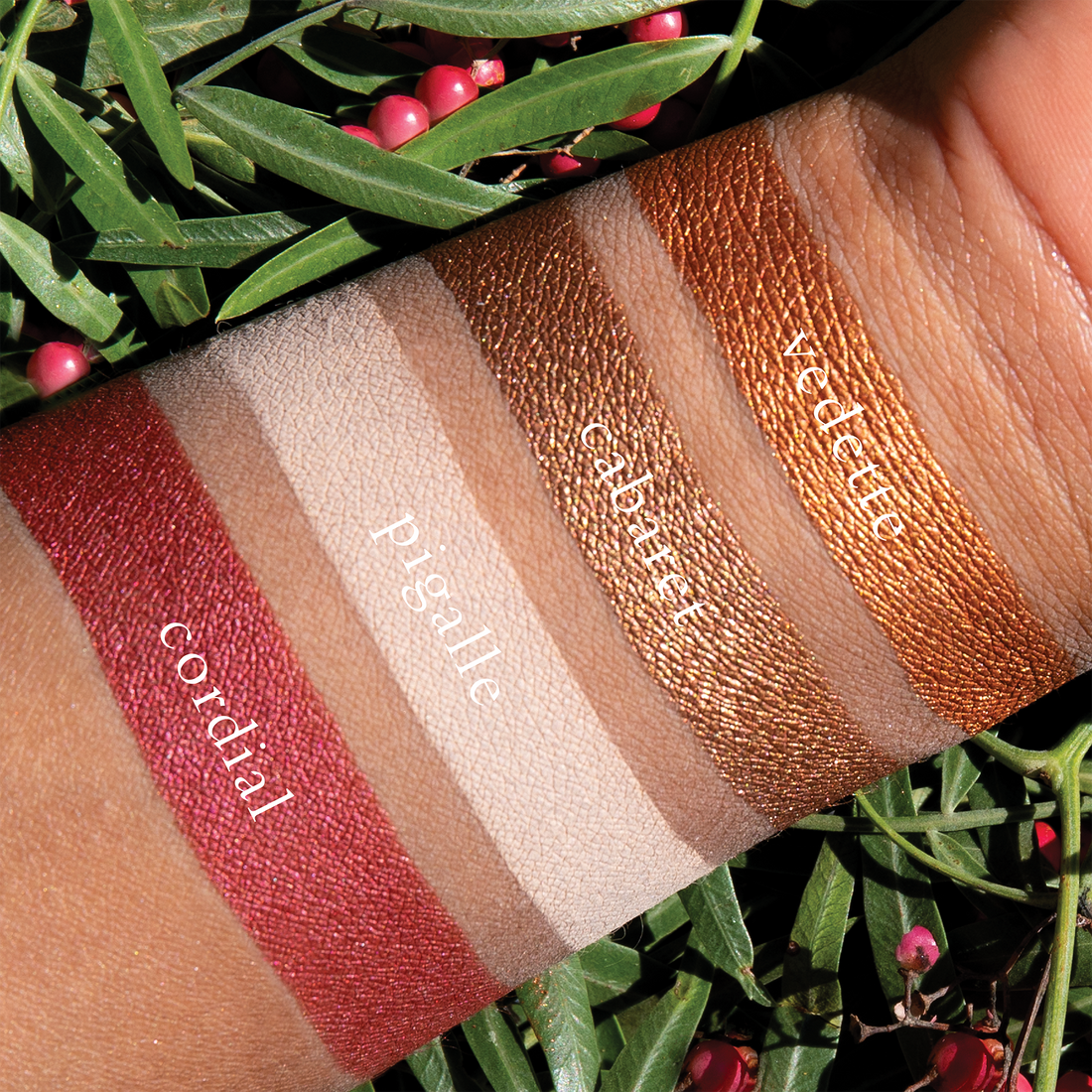 Swatches of Petits Fours Garnet on deep skin, highlighting warm red matte, plum shimmer, and wine satin.